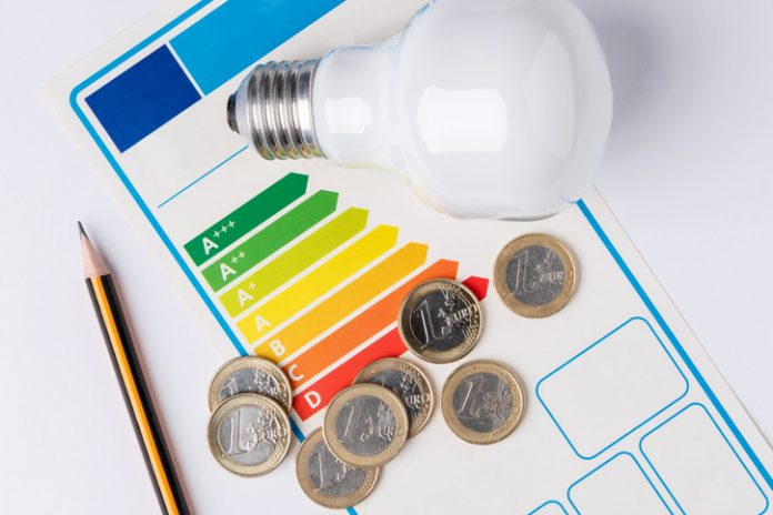 Energy efficiency scale with a light bulb, a pencil to make calculations and coins representing the cost of energy